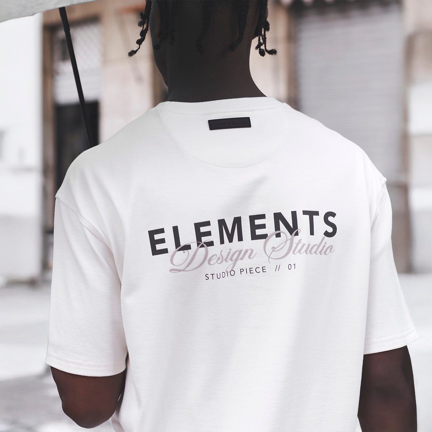 Person wearing a white t-shirt with 'ELEMENTS Design Studio' text on the back.