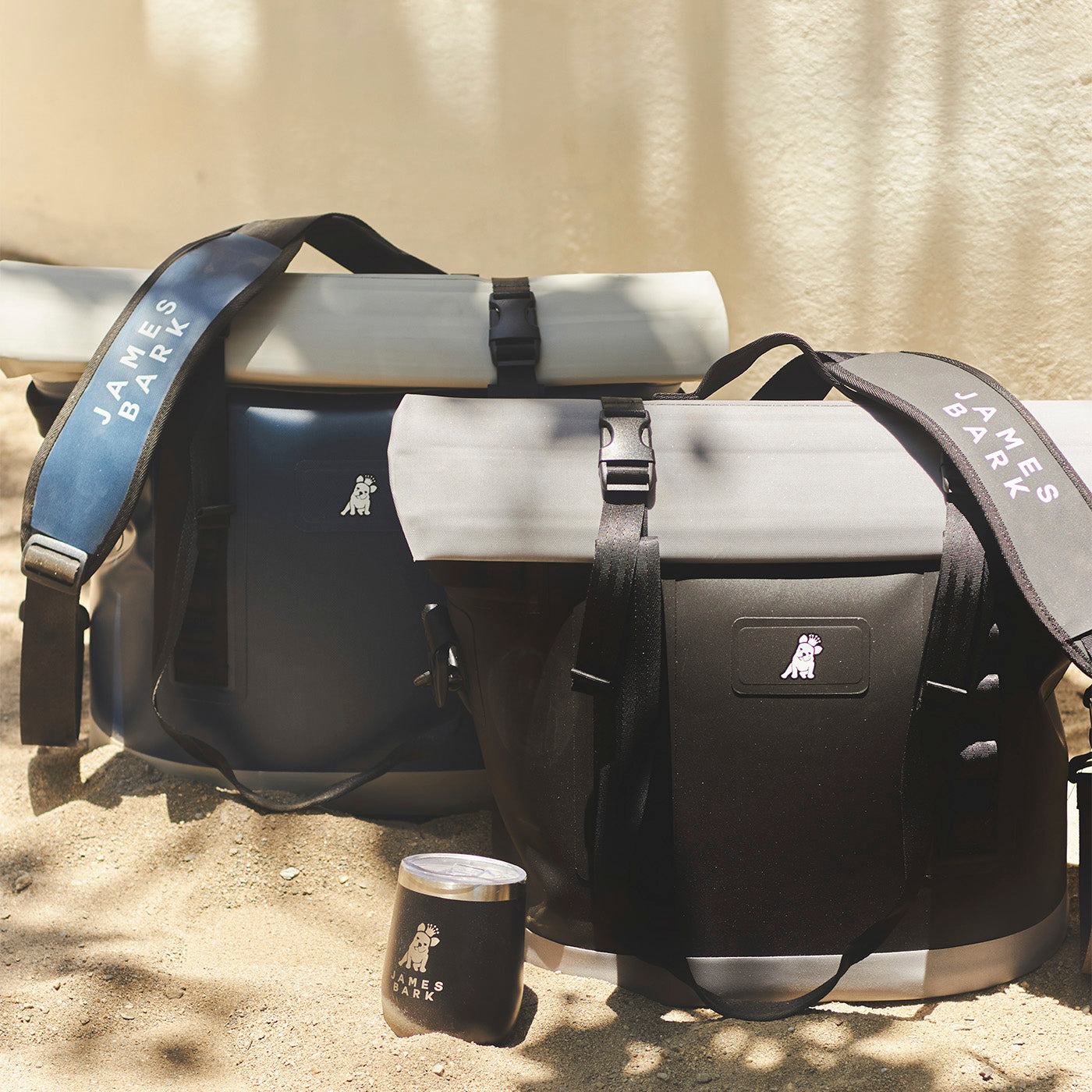 Black and gray cooler bags placed on a sandy surface.