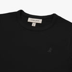 A close-up of a black short-sleeve T-shirt, showing the ribbed crewneck collar and finely knit fabric texture. The white neck label displays the brand name "JAMES BARK" with "Est. 2015" beneath it, along with the size "S." A subtly embroidered logo of a dog, matching the black fabric, is positioned on the left chest area. The material appears soft and high-quality.