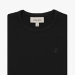 A close-up of a black short-sleeve T-shirt, neatly folded to showcase the ribbed crewneck collar and finely knit fabric texture. The white neck label displays the brand name "JAMES BARK" with "Est. 2015" beneath it, along with the size "S." A subtly embroidered logo of a dog, matching the black fabric, is positioned on the left chest area. The material appears soft and high-quality.