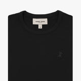 A close-up of a black short-sleeve T-shirt, neatly folded to showcase the ribbed crewneck collar and finely knit fabric texture. The white neck label displays the brand name "JAMES BARK" with "Est. 2015" beneath it, along with the size "S." A subtly embroidered logo of a dog, matching the black fabric, is positioned on the left chest area. The material appears soft and high-quality.