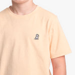A close-up of a person wearing a light peach T-shirt with a small black and white dog on the left chest, set against a white background.