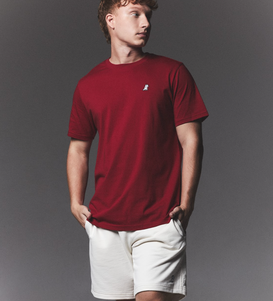 Man wearing a red t-shirt and white shorts against a gray background