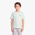 A boy wearing a light mint green T-shirt with a small black graphic on the left chest, paired with light gray shorts