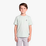 A boy wearing a light mint green T-shirt with a small black graphic on the left chest, paired with light gray shorts