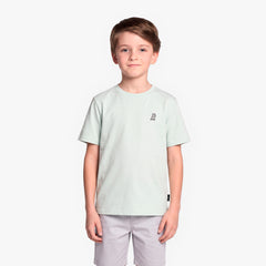 A boy wearing a light mint green T-shirt with a small black graphic on the left chest, paired with light gray shorts