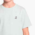 A close-up of a person wearing a pale mint green T-shirt with a small black dog on the left chest, set against a white background.
