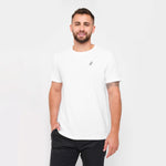 A man with a beard standing, wearing a white T-shirt, smiling with his hand in his pocket, paired with black pants.