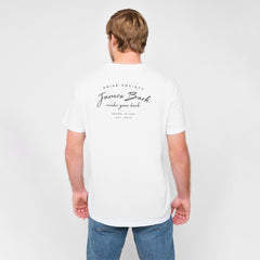 A man standing with his back to the camera, wearing a white T-shirt with black text on the back, paired with jeans.