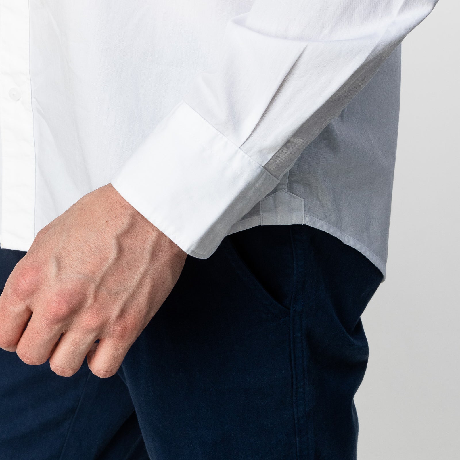 Close-up of the sleeve of the white button-up shirt: The image focuses on the cuff and the man's hand as he adjusts his sleeve.