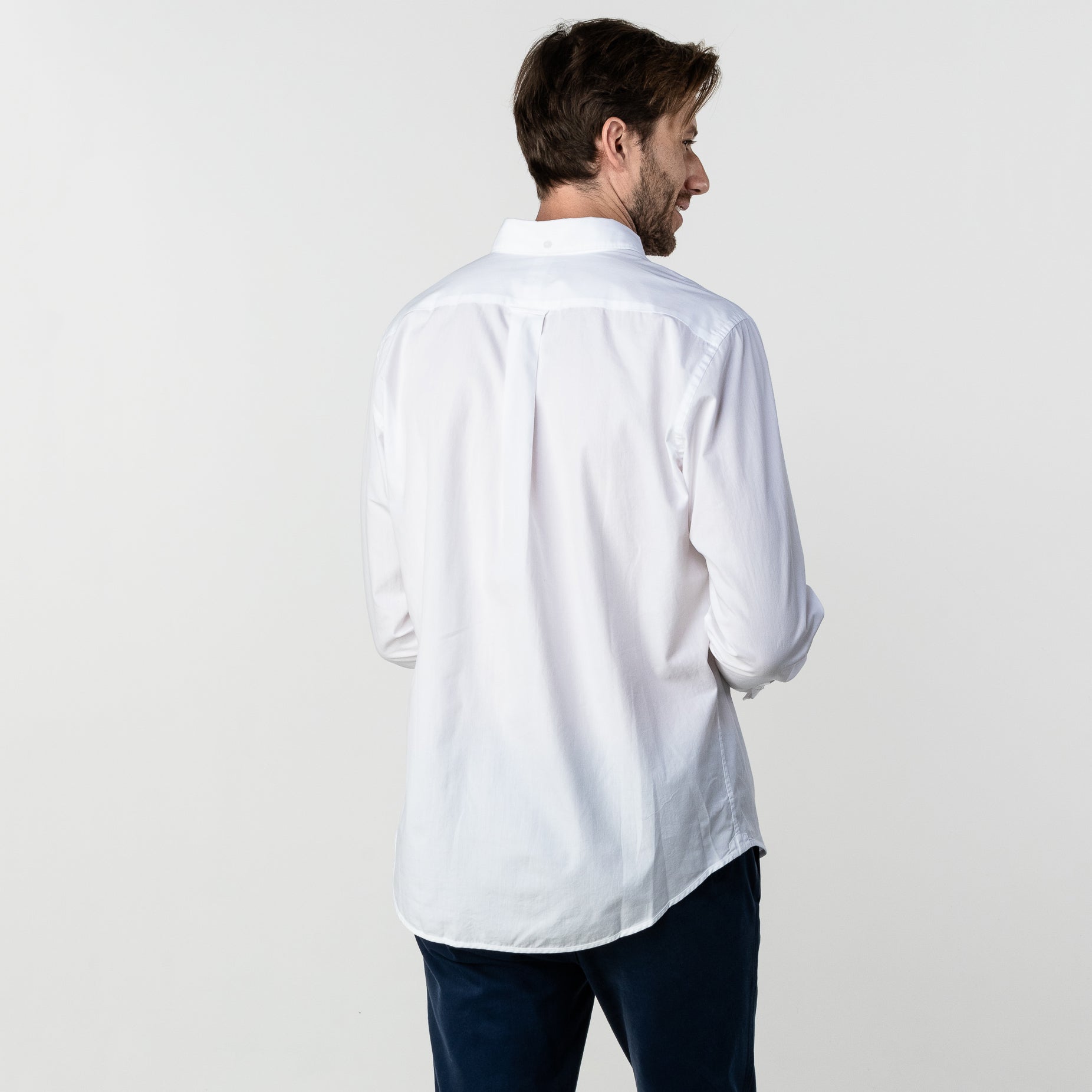 Back view of a man wearing the white button-up shirt: The man is standing with his back to the camera, showing the back fit and length of the shirt.