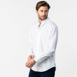 Front view of a man wearing a white button-up shirt: The man is standing with a casual pose, adjusting the sleeve of his white shirt. He is wearing dark pants.