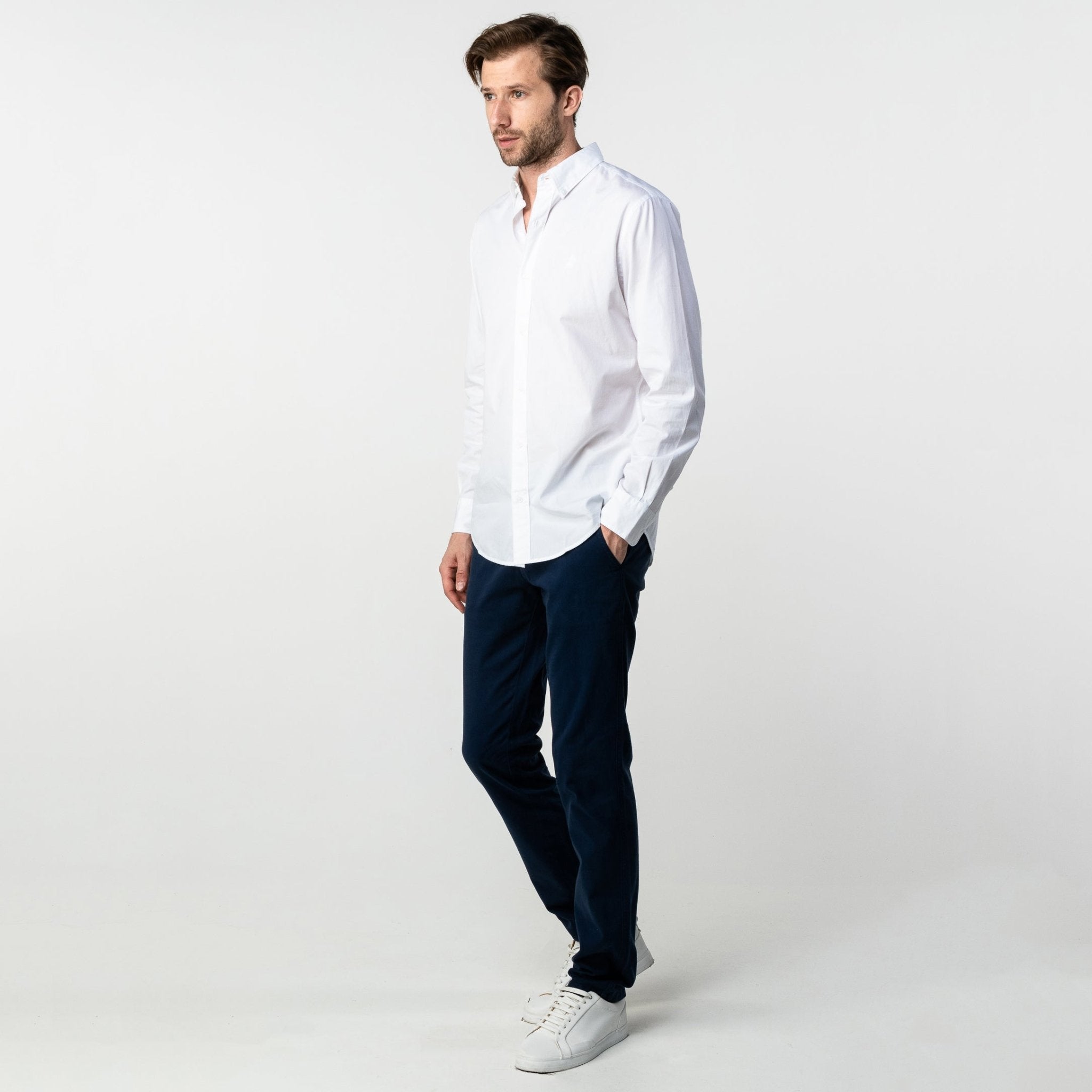 Full-body view of a man wearing the white button-up shirt and dark pants: The man is standing with one hand in his pocket, showing the full outfit from head to toe.